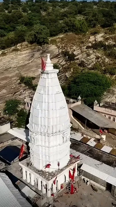 The white shikhar of the Jeen Mata temple with red flags, against the rocky Aravalli hillside